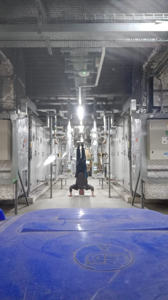 a video still of the artist in a headstand position in  the service area of his workplace