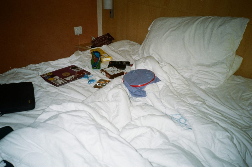 a photograph of an unmade bed with a laptop, sewing and remote on it. 