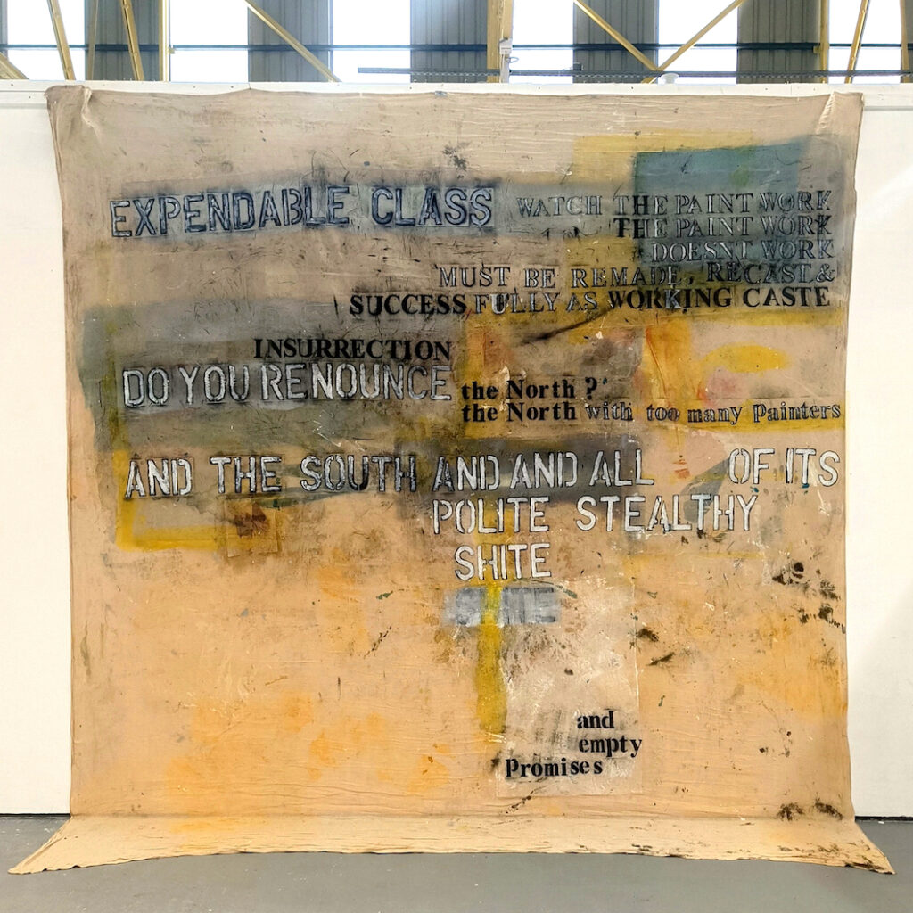 a canvas hangs on a wall and touches the ground. On it is paint and some text