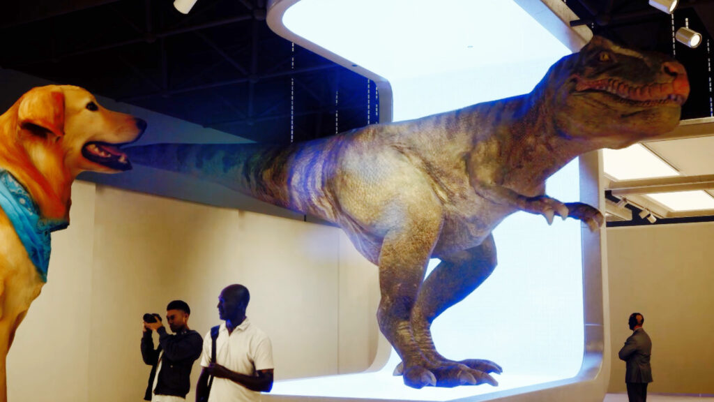 An image of large sculptures of a dog and dinosaur with people stood viewing and photographing them 
