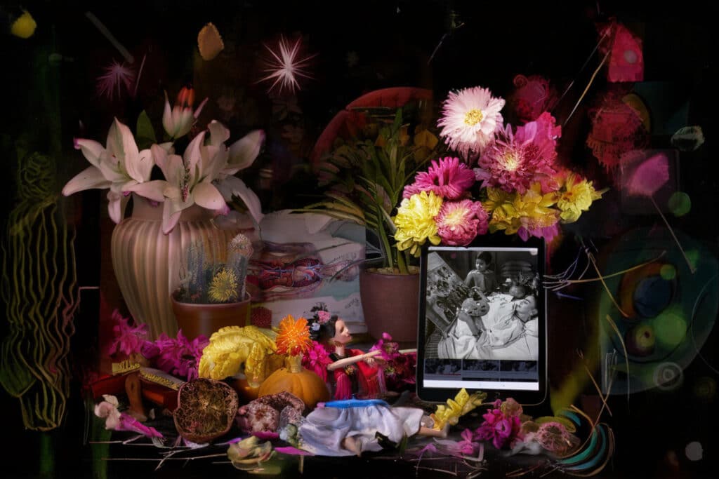 Photograph of a still life of flowers, fruit Barbie doll and photo of a women in a bed.