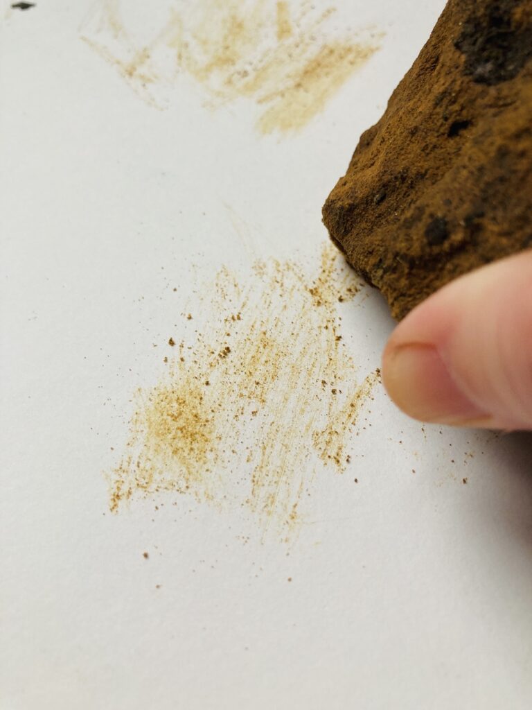 Image of a hand drawing with a rock that leaves a yellow mark on the paper