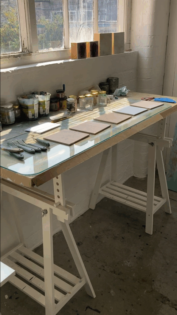 photograph of artist's studio with table with square boards on it ready to be painted.