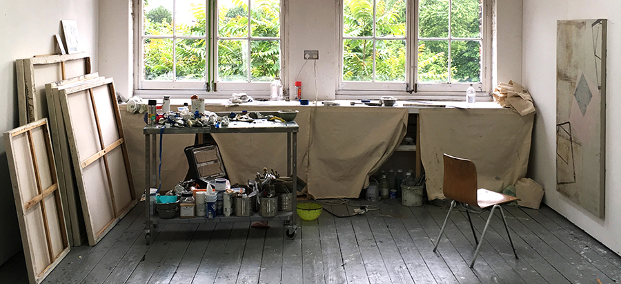 Interior of artist studio including table, chair, canvases and trolley with painting materials