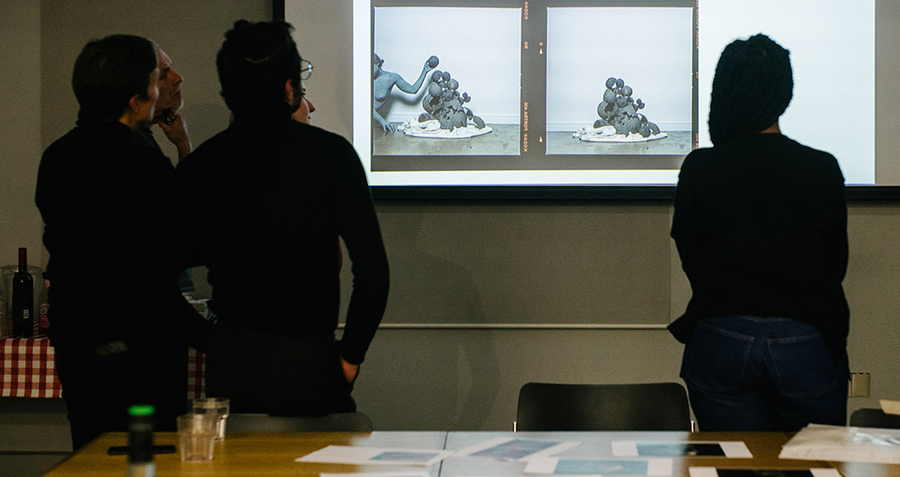 Five people looking at images projected on a wall, their back turned to the camera