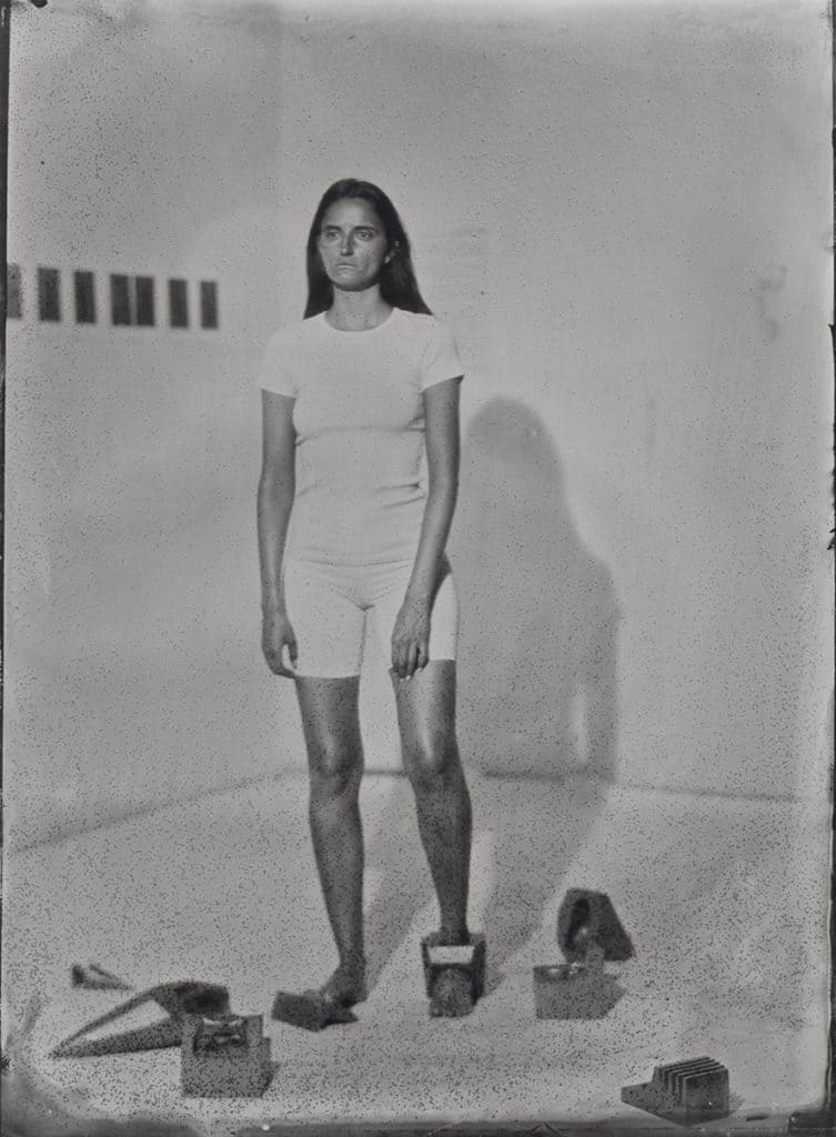 Black and White photograph of a women dressed in white with wearable drawing devices attached to her feet and surrounding her