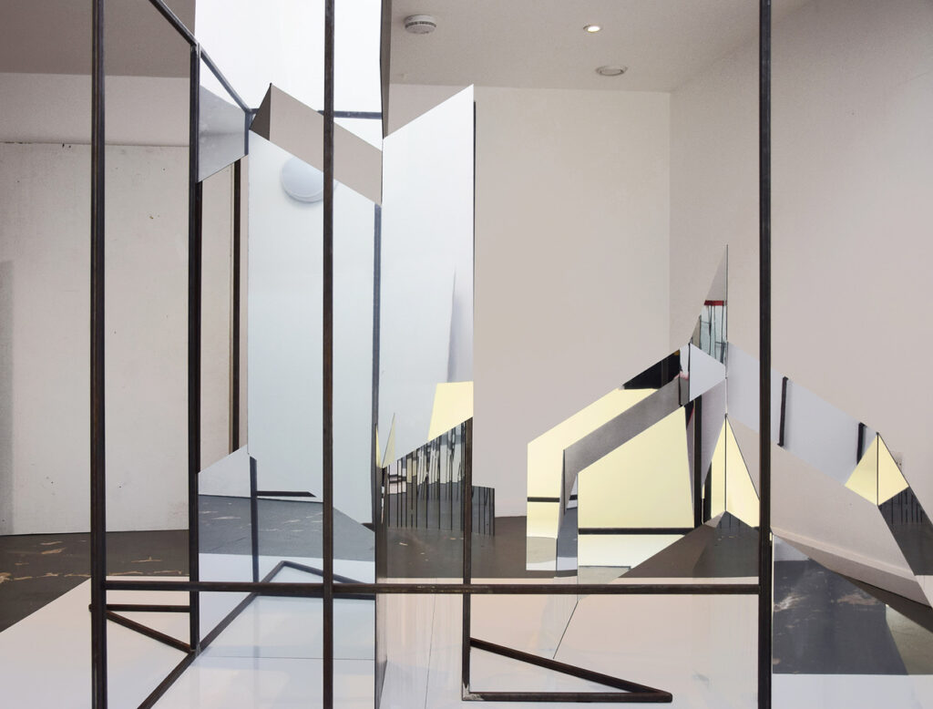 photograph of a structure in a white walled gallery made from steel angle and angled pieces of mirror