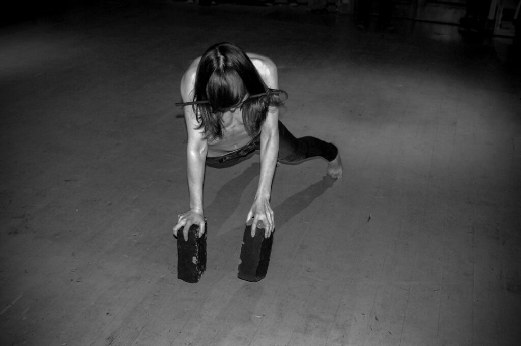 black and white photograph of a person  holding a brick in each hand to balance on all fours. 