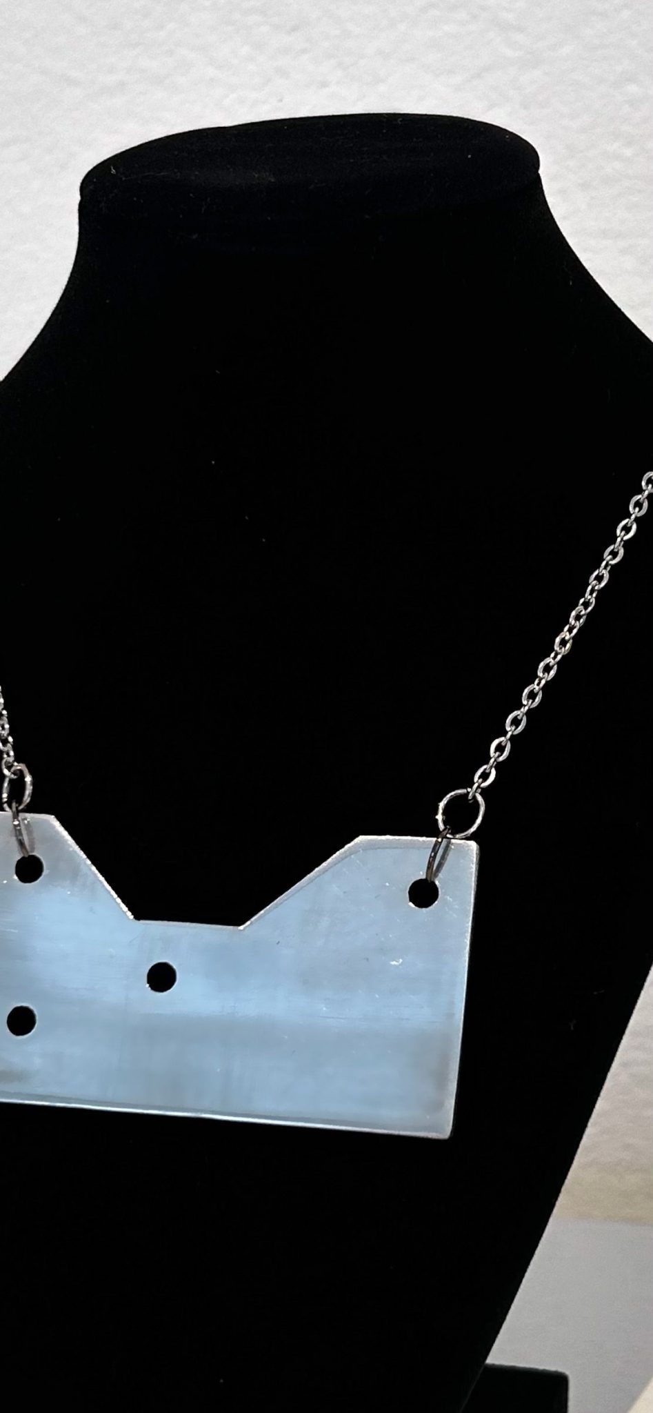 cropped image of an steel necklace with an aluminum pendant. The pendant is in the shape of a galvanized steel framing angle. The necklace is on a velvet necklace bust display stand.