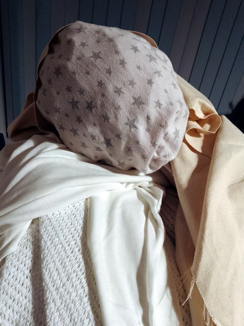 A vaguely head-shaped fabric sculpture made from a white pillowcase with grey stars printed on it. The head is surrounded with cream canvas and layered white cellular blankets.