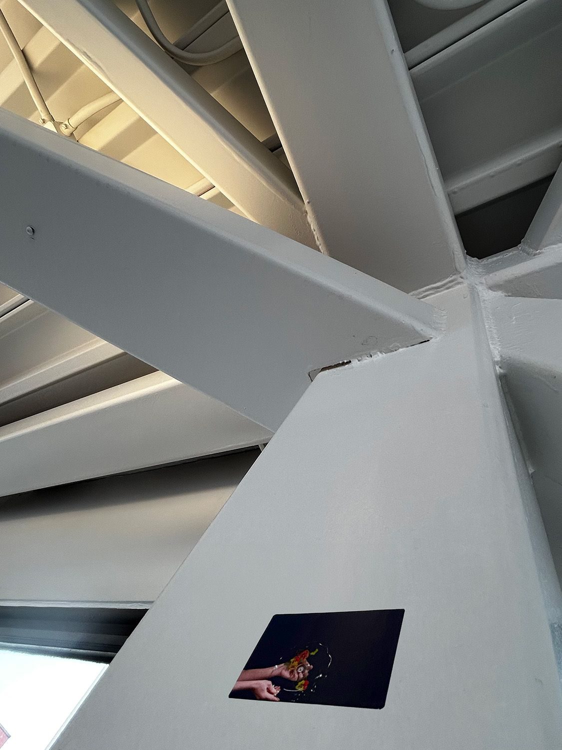 sticker of artists hands holding a plate with a navy background a fixed on structural beams inside a sky walkway