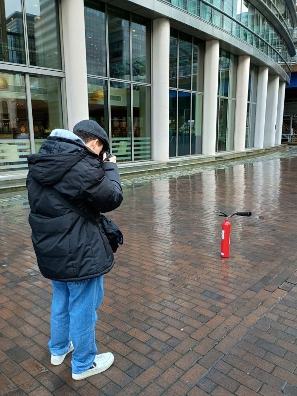 Man photoghing an abandoned red carbon dioxide fire extinguisher outside a restaurant