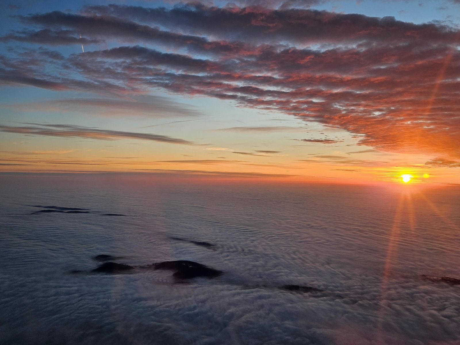 An aerial photo of the sun rising over a cloud bank.