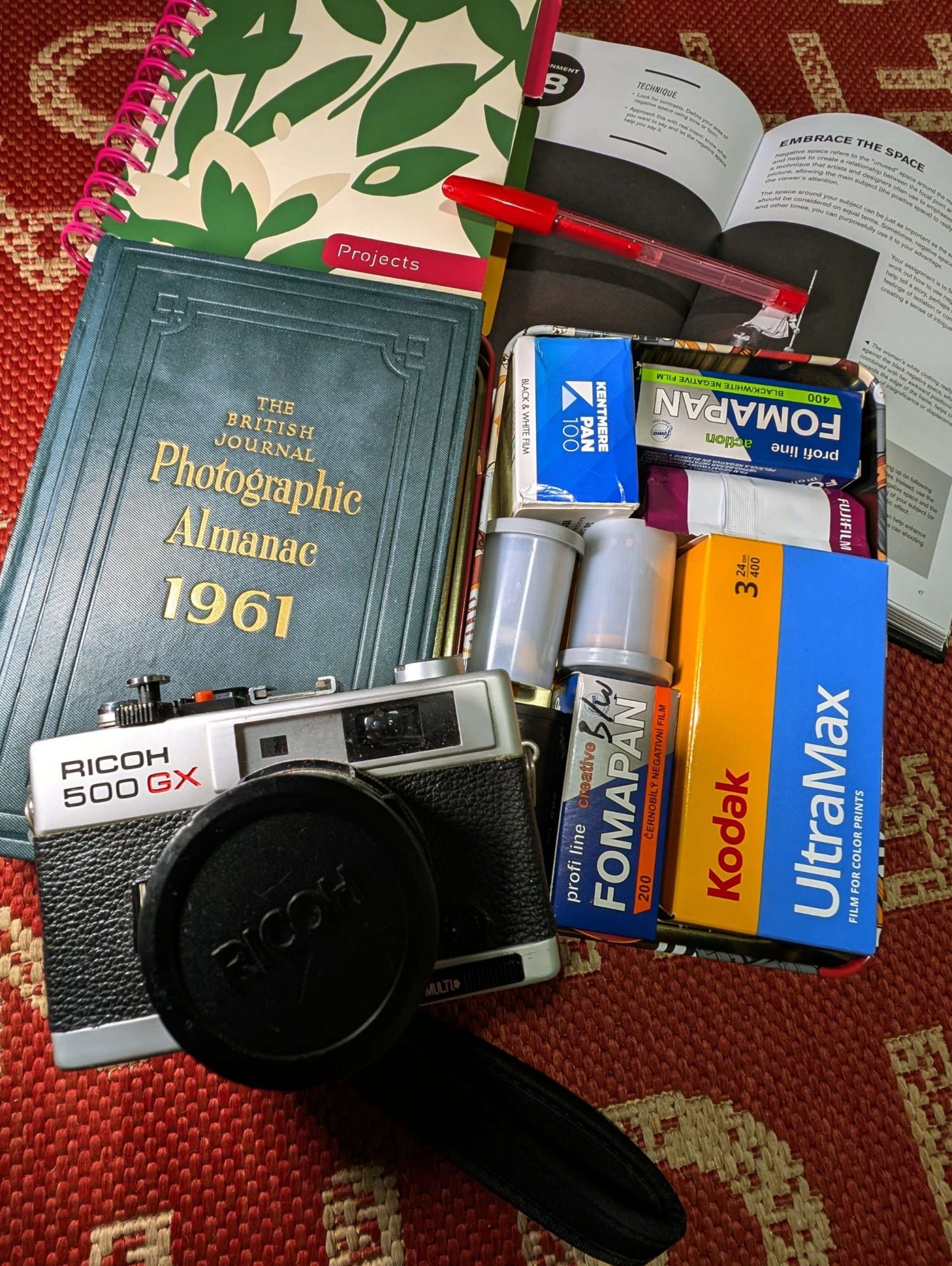 Still life of a notebook, box of film, a Ricoh 35mm camera and two photography books