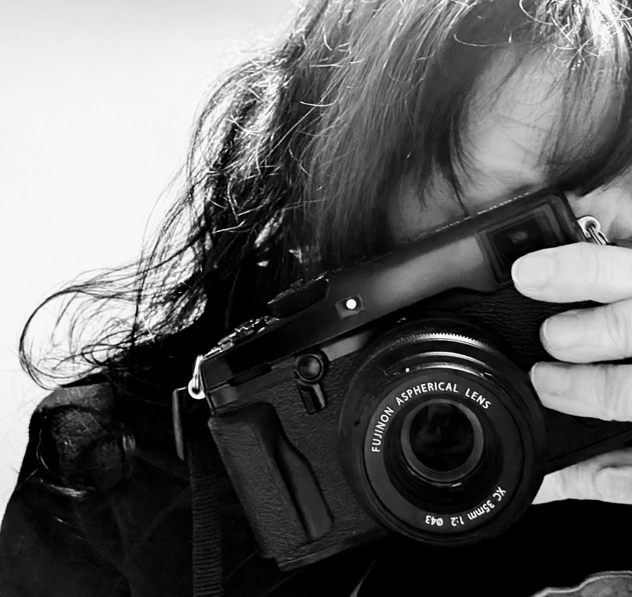 Black and white self portrait of a black haired woman holding a black camera to her eye