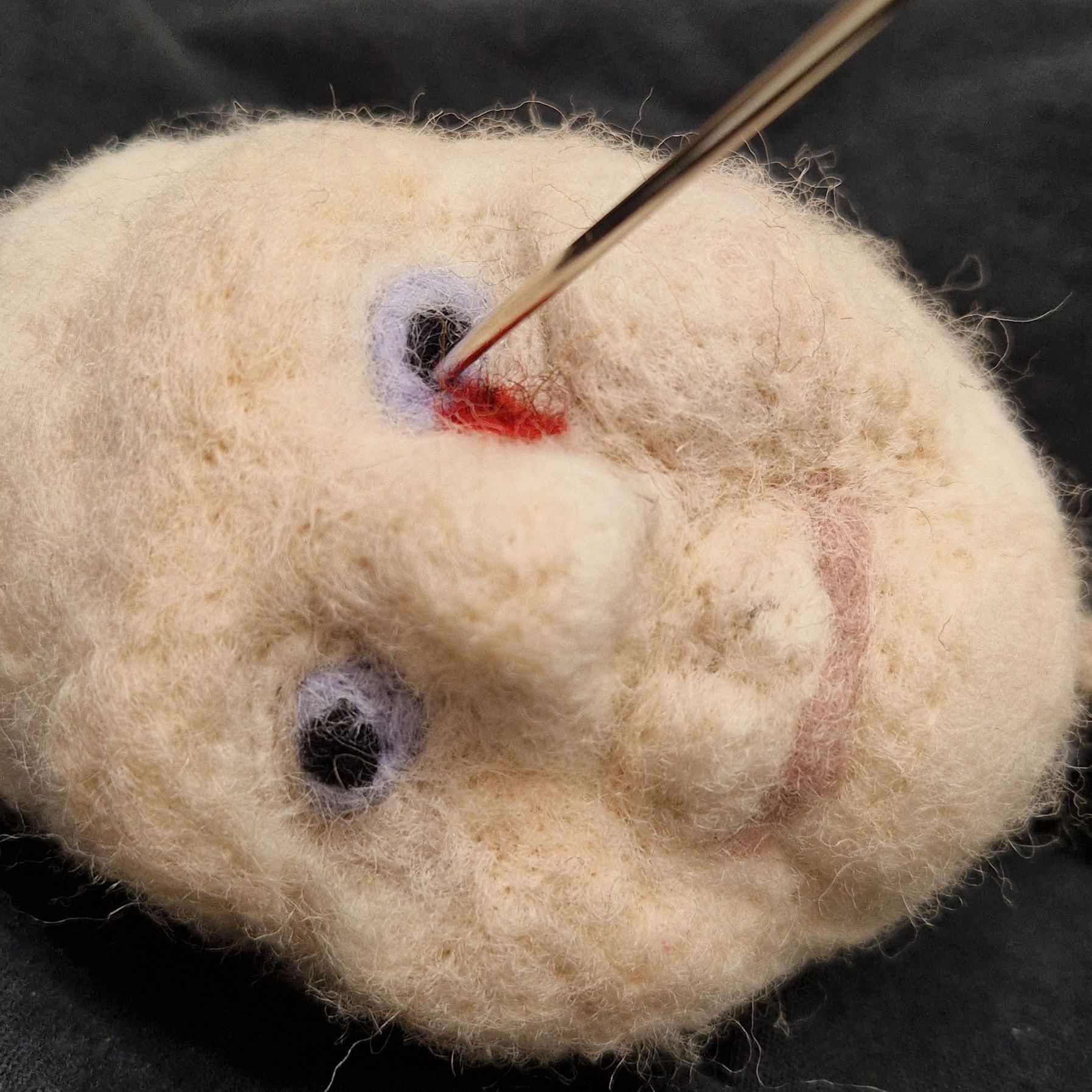 Needle felted head of an old lady with a needle through her left eye