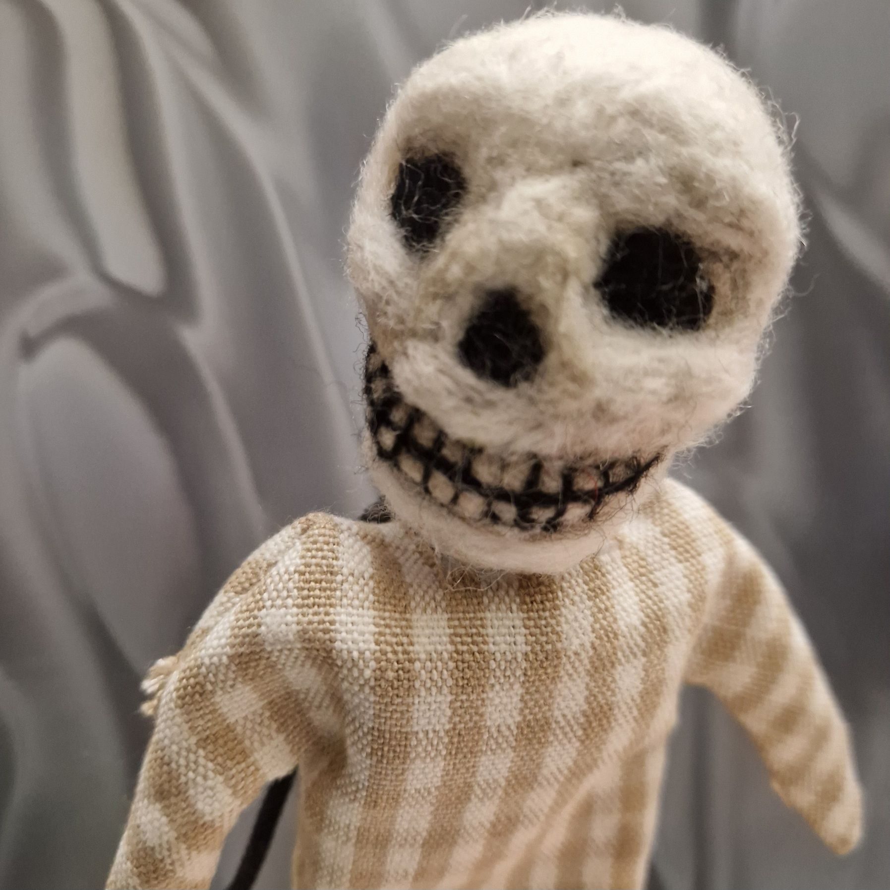 Needle felted skeleton in a pale beige and white checked dress.