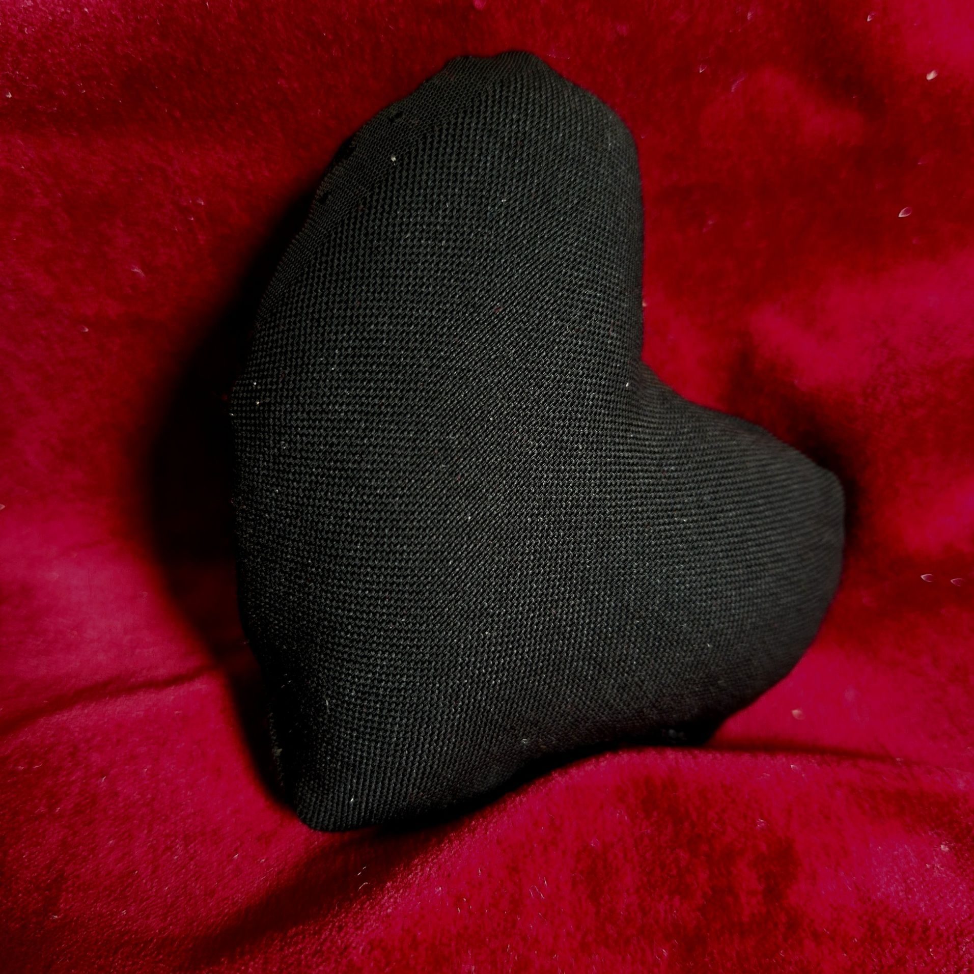 Black heart-shaped cushion on red velvet draping
