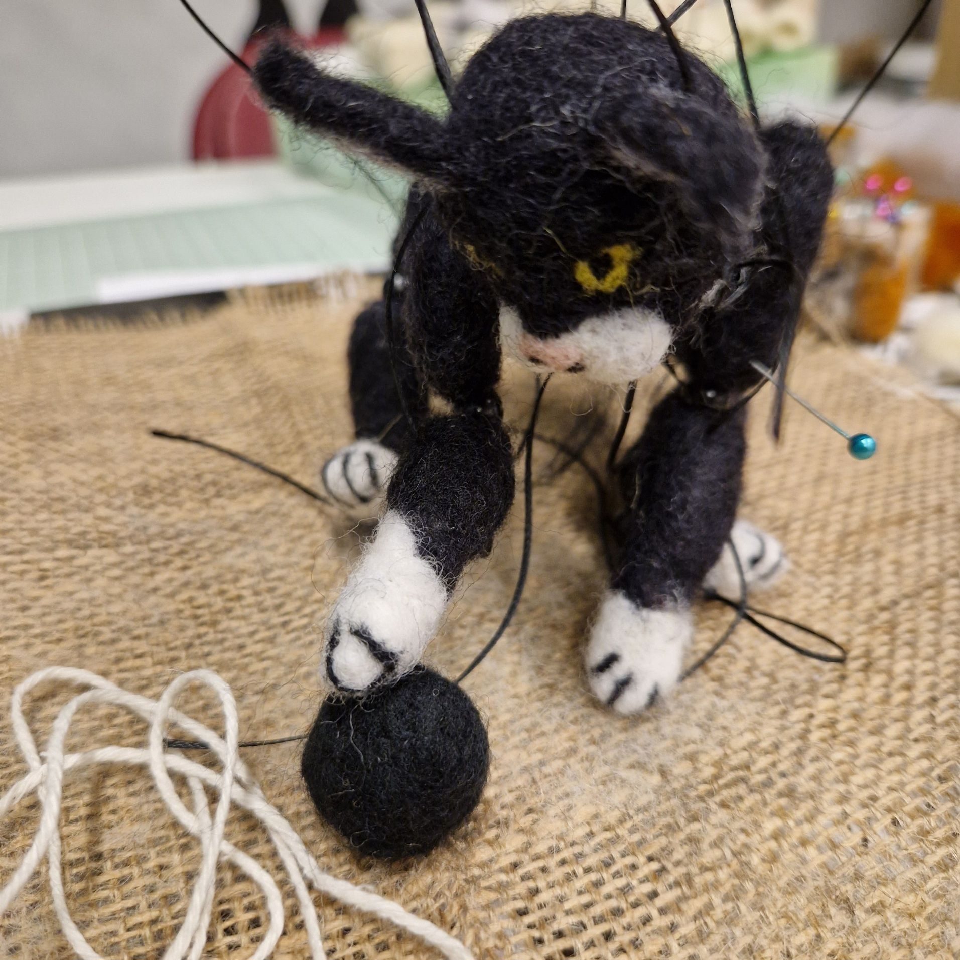 Black and white needle felted cat marionette playing with a black woolen ball.