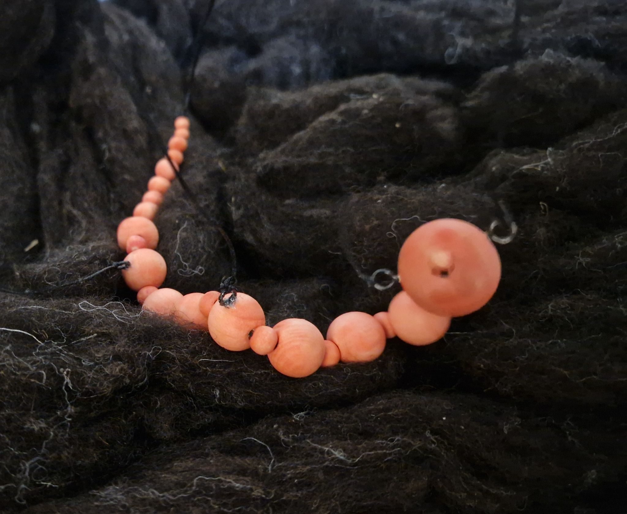 Pink wooden worm marionette on dark wool background resembling soil