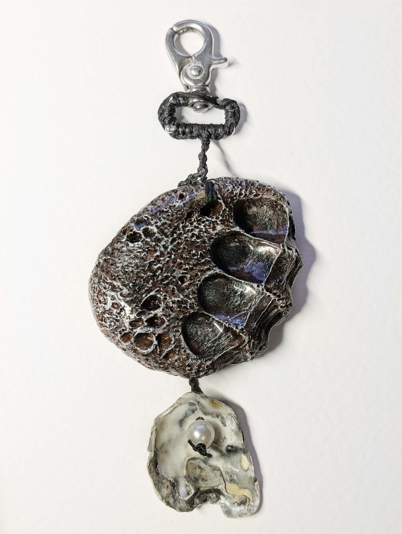 A bag charm made of clay and shell, looking like lava rock with fingers indentions.