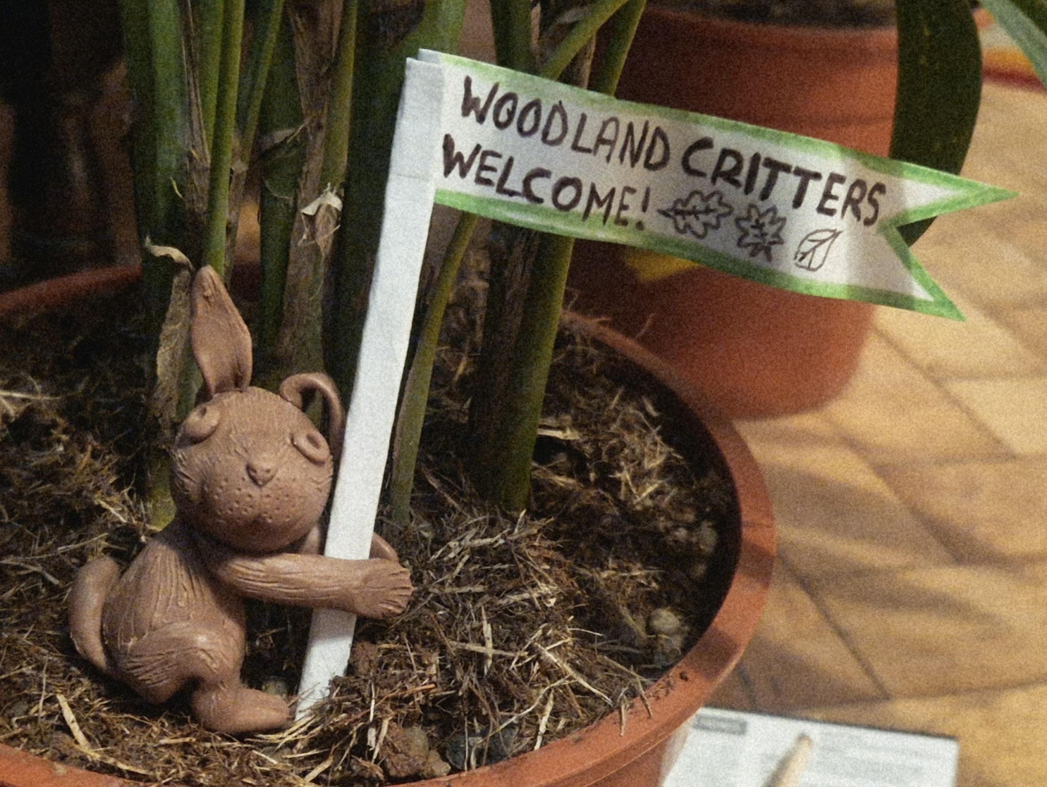 A brown clay molded rabbit sits looking at the camera holdinf a flag pole witb a swallowtail cut long flag that reads 