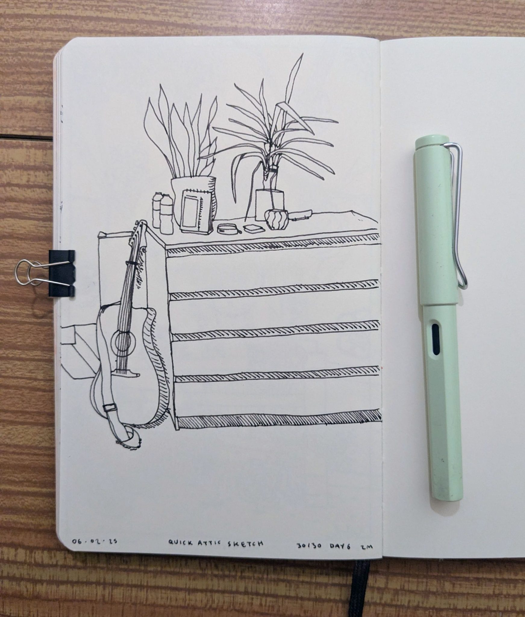 Photograph of a sketchbook page showing a black ink sketch of a set of drawers, guitar and knick knacks