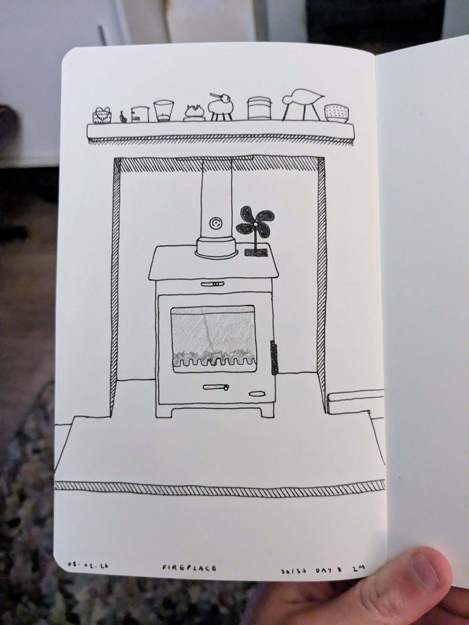 Photograph of a sketchbook page showing an ink drawing of a fireplace
