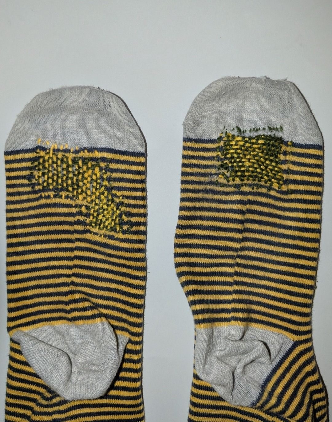 Photograph of the top soles of navy and yellow striped socks. Socks have been darned using dark green and yellow thread.