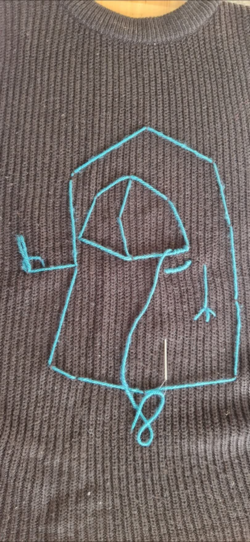 A little Cyclops throwing profanities, sewn onto a knitted sweater vest.