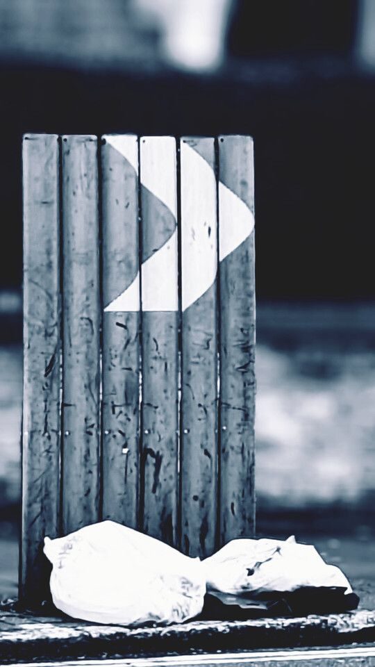 A large unusual street sign with an arrow pointing to the right side, and bin bags in front of it. In grey tones
