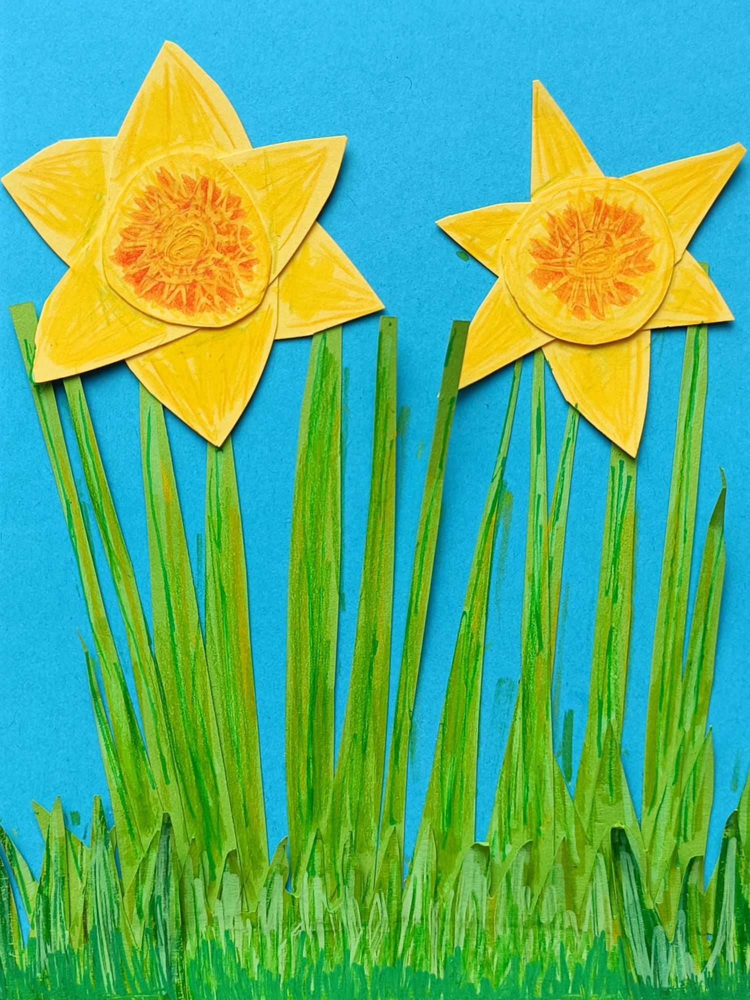 a paper cut collage of two daffodils surrounded by grass, texture has been added to the paper using paint pens and pencils