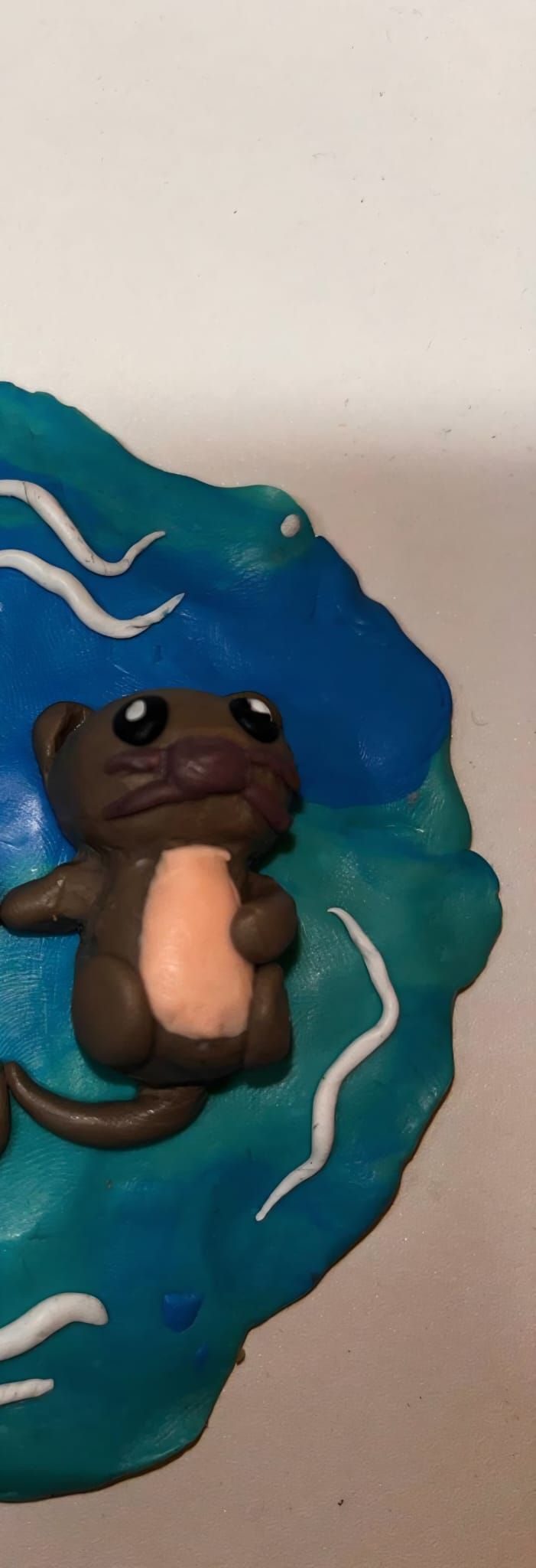 A polymer clay otter floating on clay water, cropped down the middle
