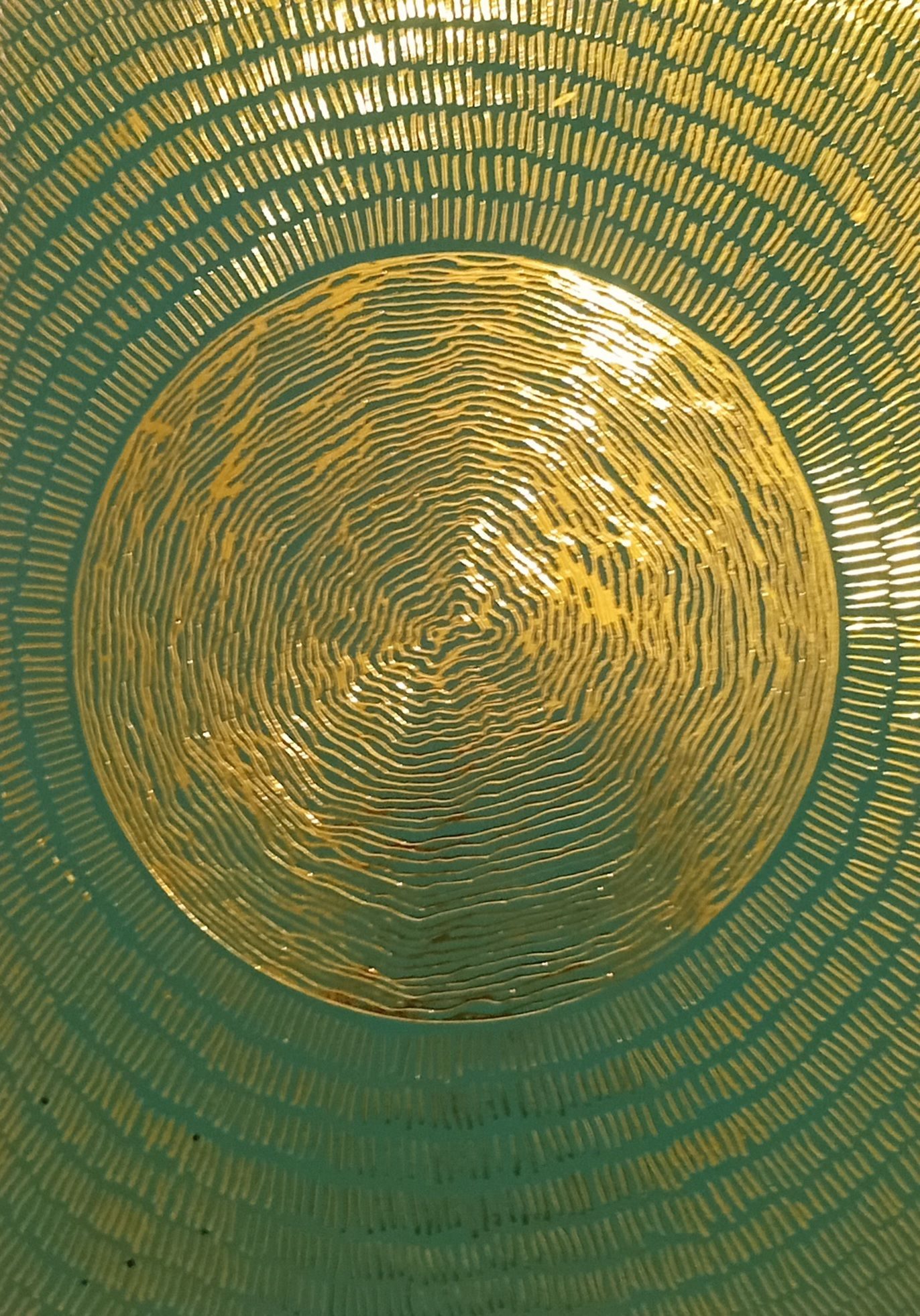 Green image with gold etched lines. Sphere in centre, circular wavy lines. Surrounded by layers of short straight lines emanating from sphere.