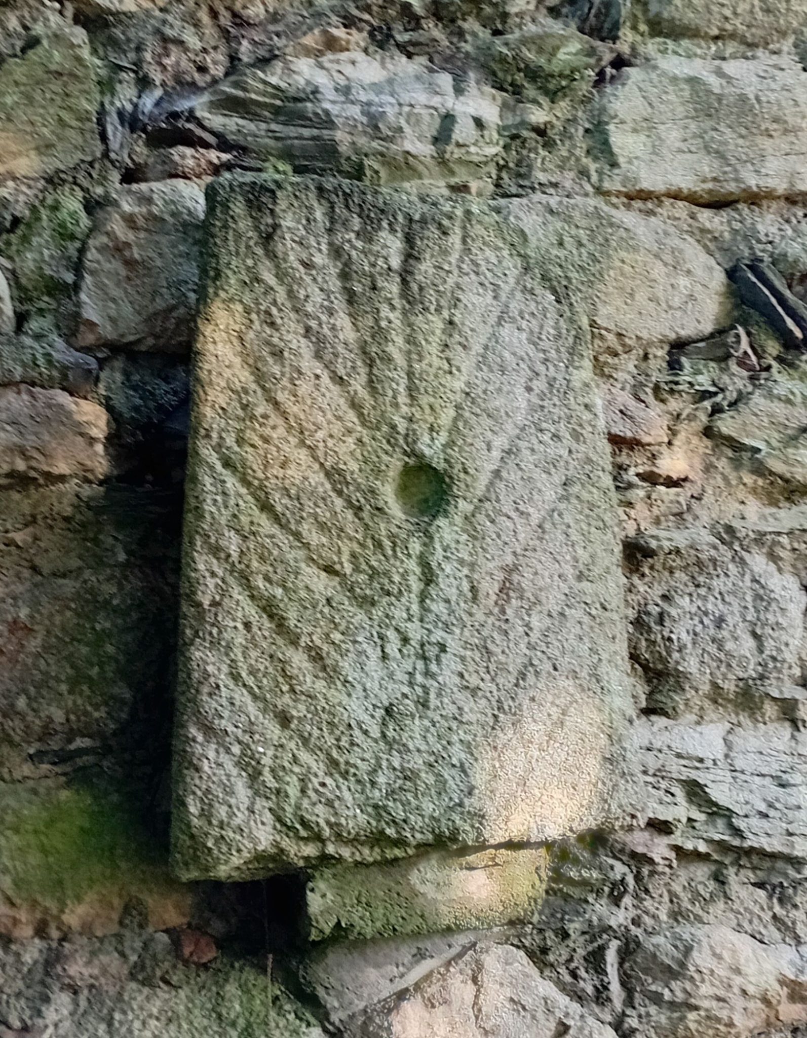 Photo of a stone slab on a brick wall. The slab is decorated with v shaped incised lines