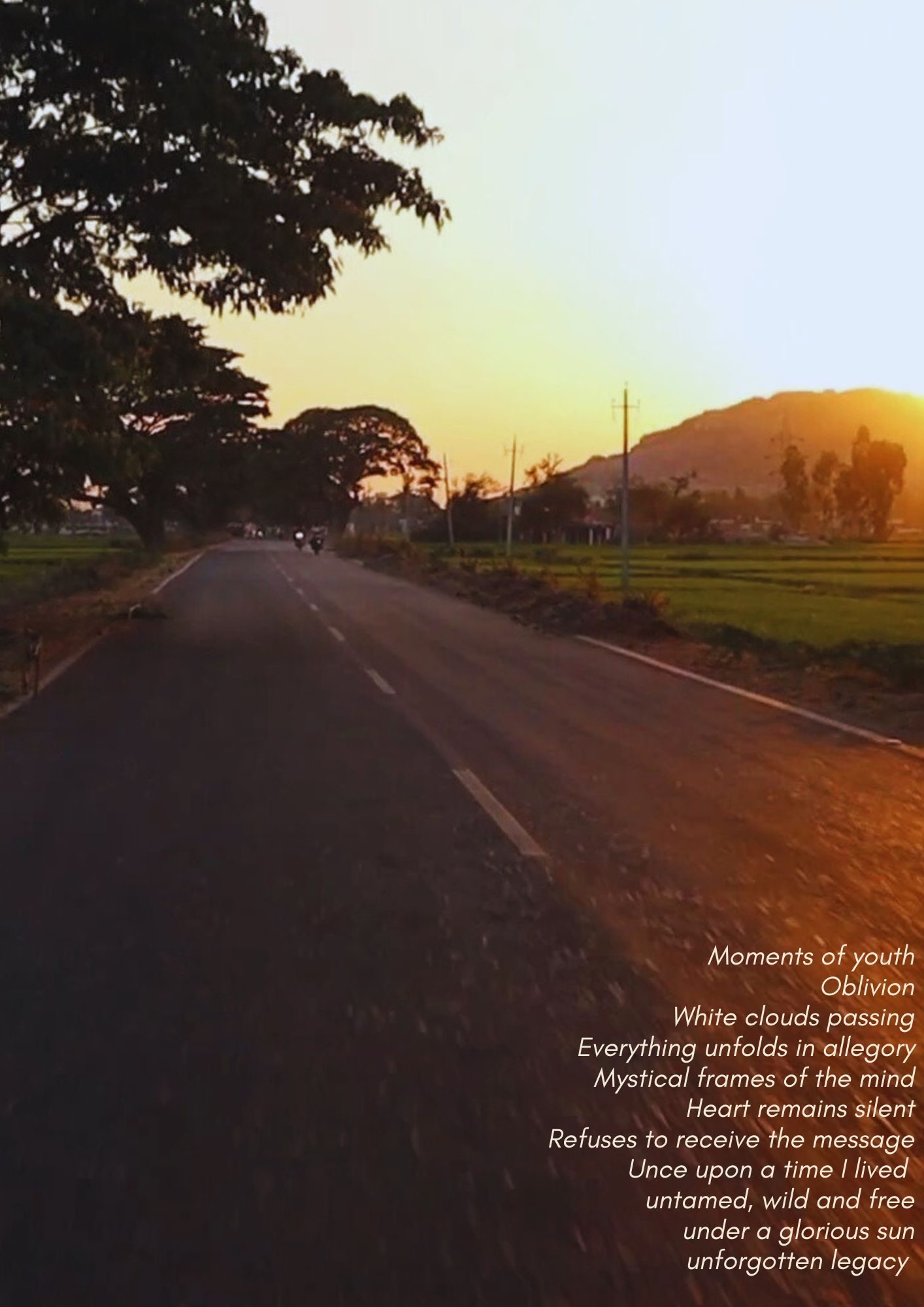A photo of a street in India. It is sunset, two motorcycles are running in the background amongst rice fields. A poem is written on the side of the frame 