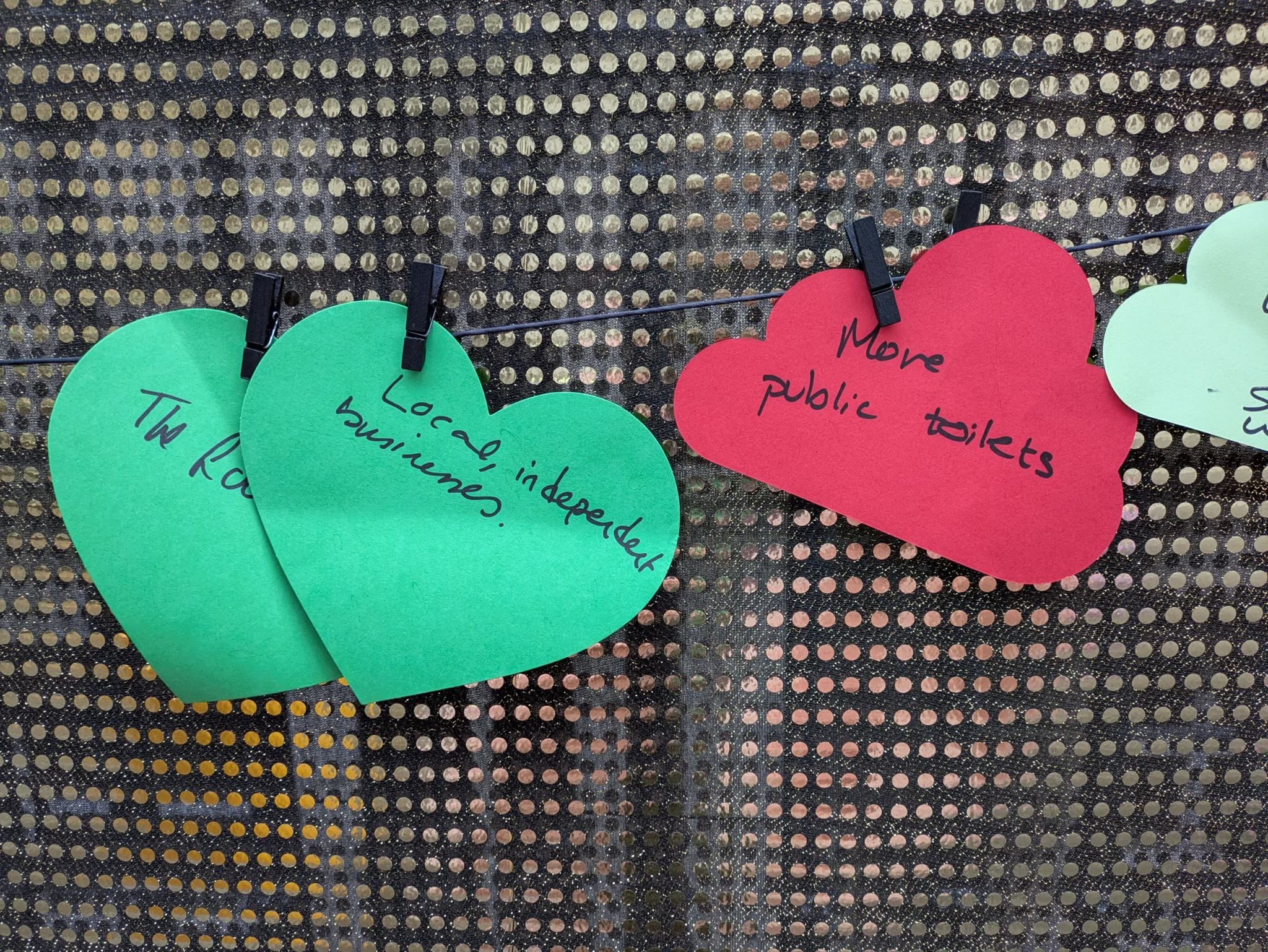 Some colourful cards in the shadow of clouds on a glittery backdrop, with comments such as more public toilets