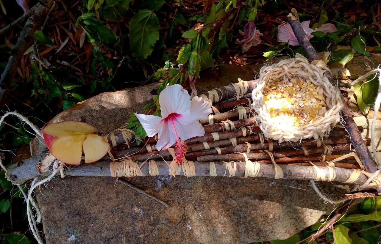 Woven platform out of protea sticks with a crocheted bowl from sisal rope for birds to feed from, hibiscus flower, piece of apple on top
