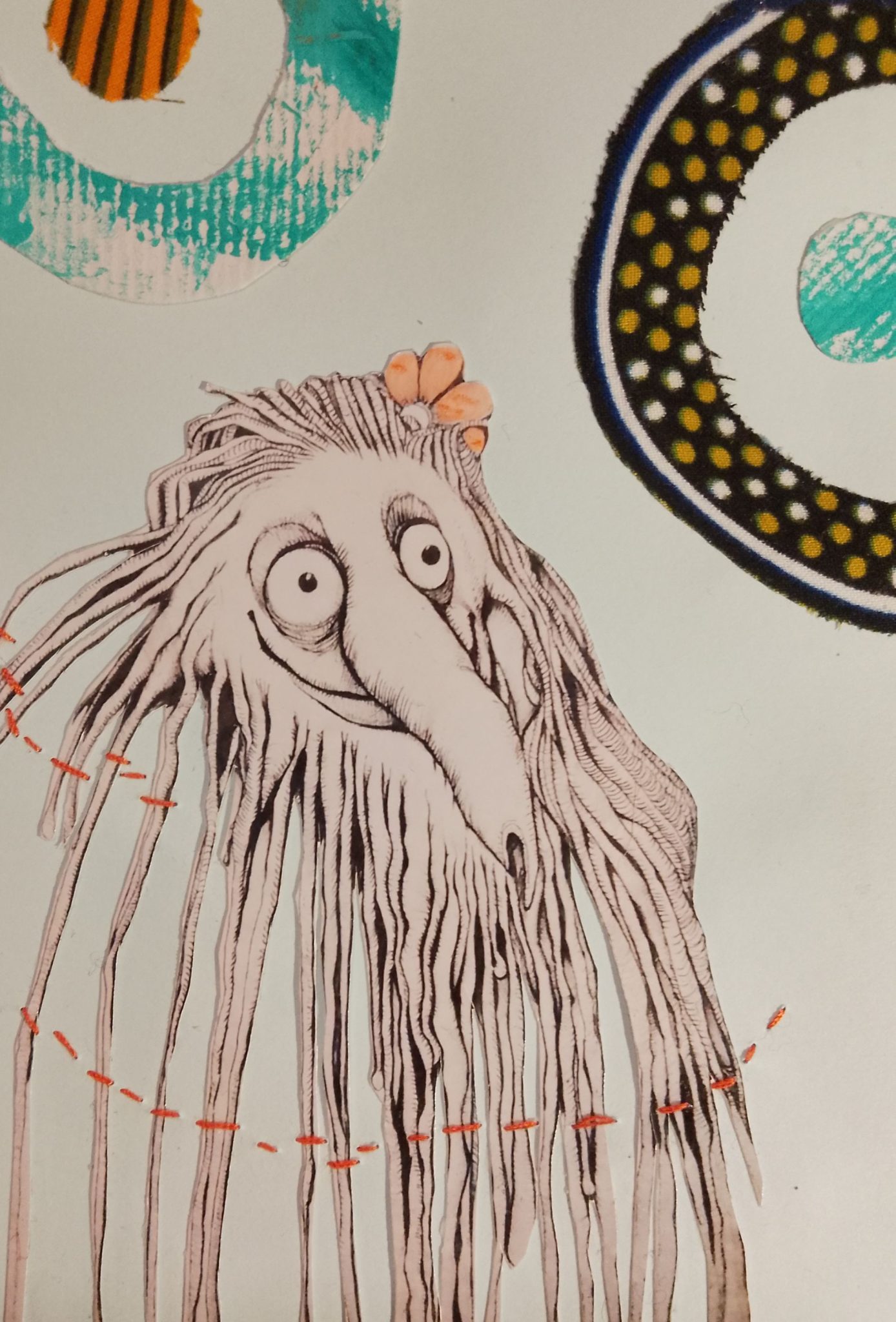 It's a mixed media collage on a light blue background, two circular sun symbols meaning a circle with a dot in the centre are on the upper left and right they are made with fabric and painted card. In the centre there is an image of a hairy creature with a smile and very long nose that looks like something growing out of a root vegetable.it is in black and white and has a pink flower hair clip. There are orange stitches going across it's hair strands that are also shaping it's beard. It's a strange creature