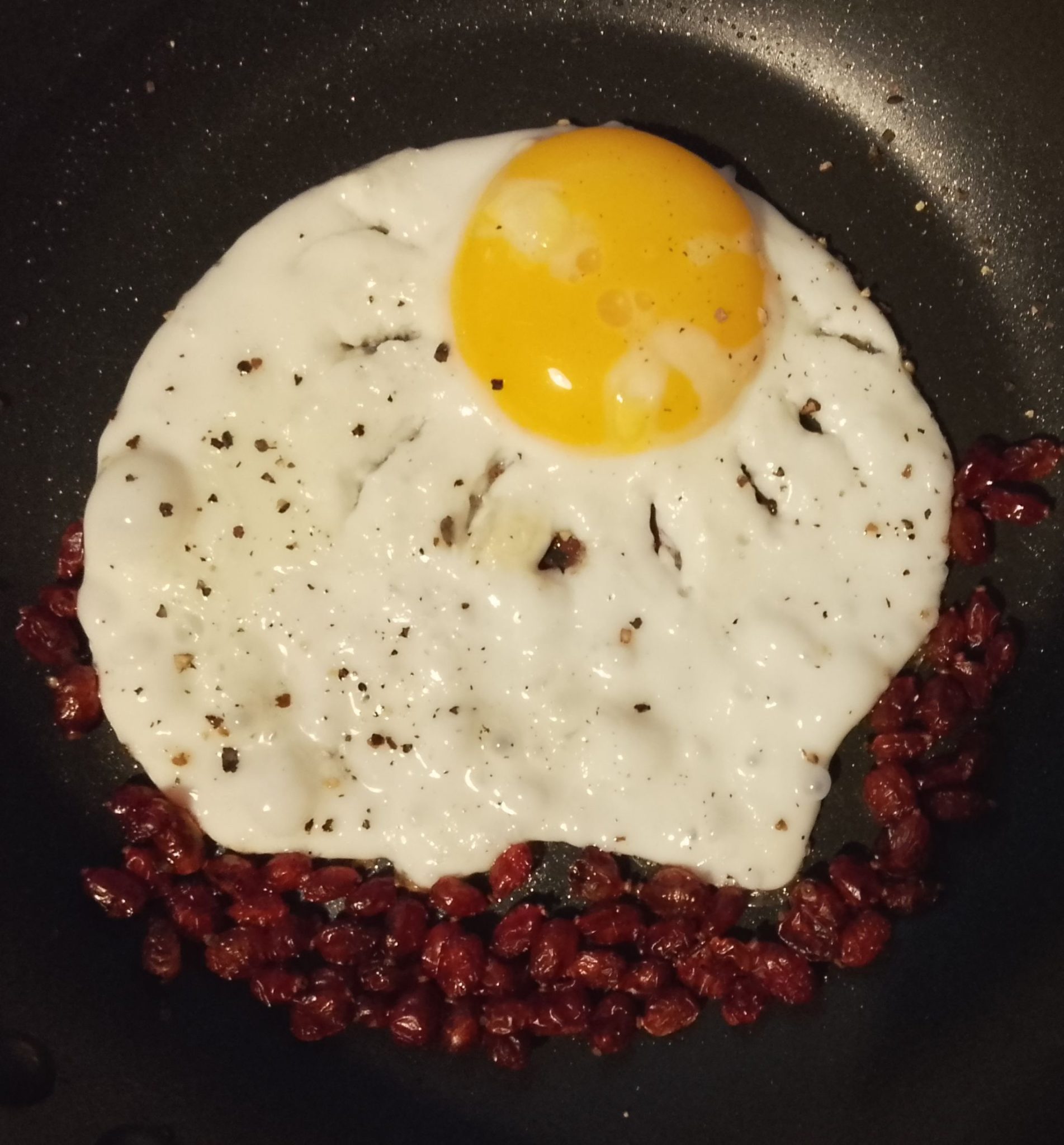 Fried egg with rays cut through the egg white making it look like the sun with barberies at the bottom