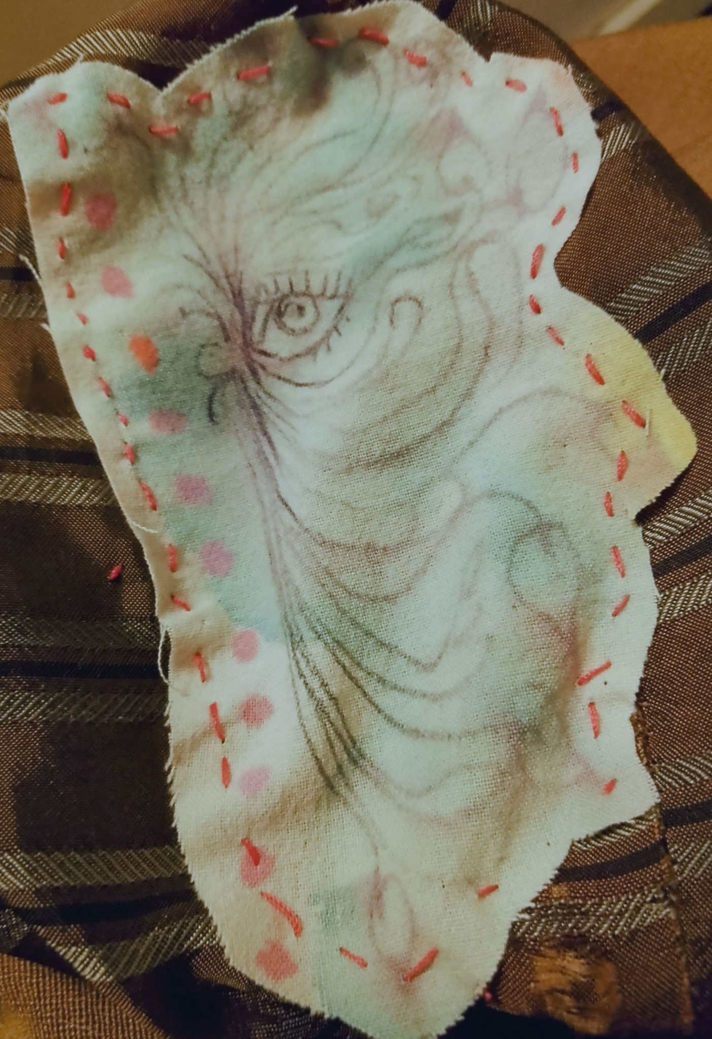 A patch made of fabric that has a pen drawing of an ye surrounded by leaves