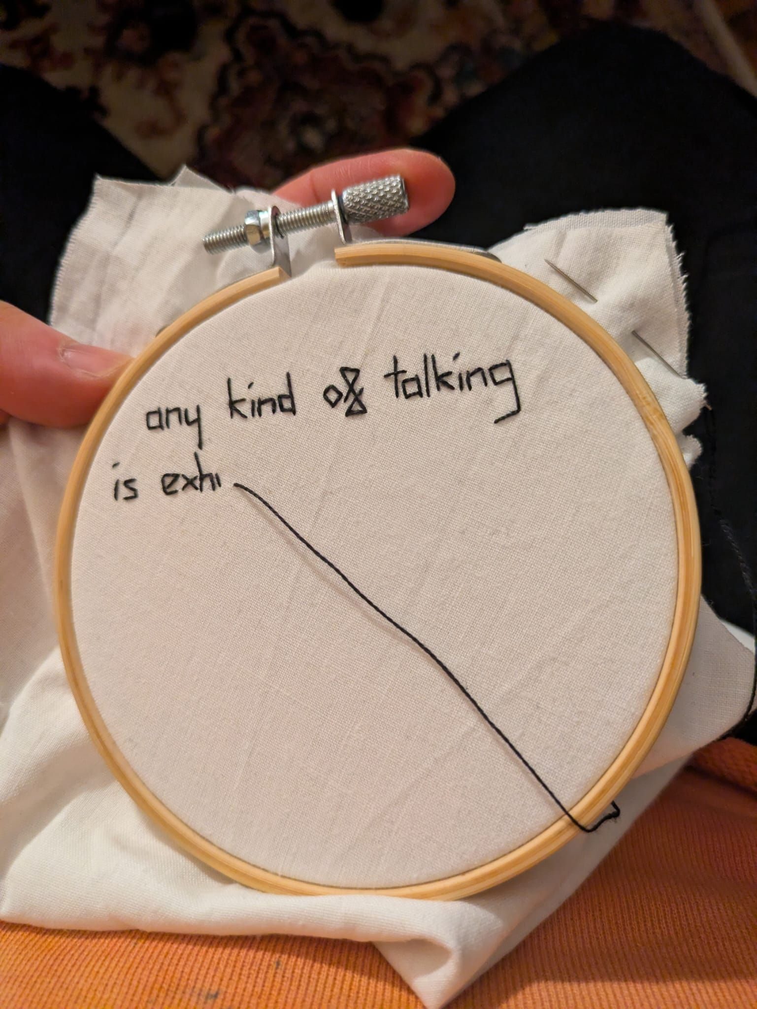 Hand stitched lettering on white fabric in a small hoop, unfinished, reading 'any kind of talking is exh'