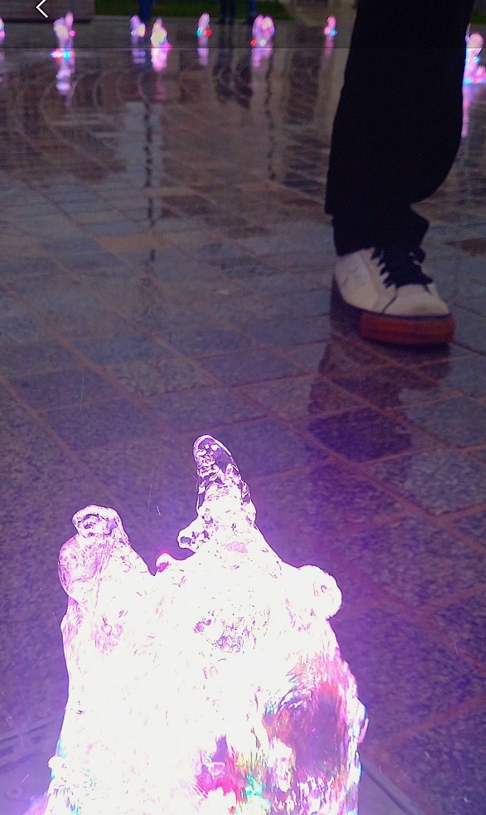 Bubbling water feature with foot walking into shot, wearing white shoes with star feature. All in saturated colours
