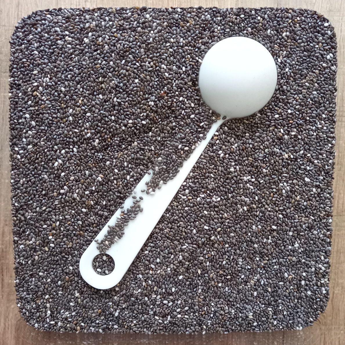 White measuring spoon partly submerged in a container of dark chia seeds
