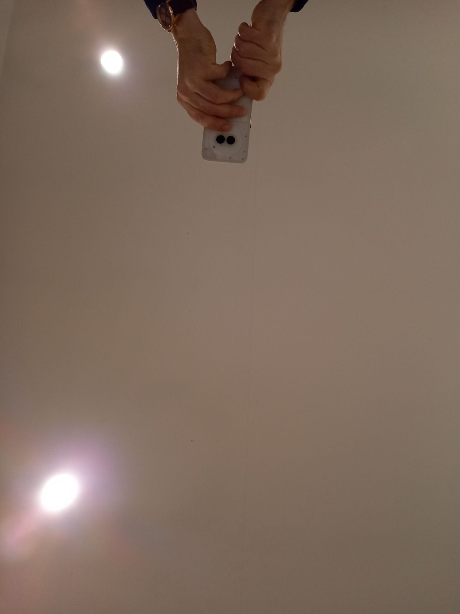 Photo of hands taking a photograph with a phone, against a white ceiling