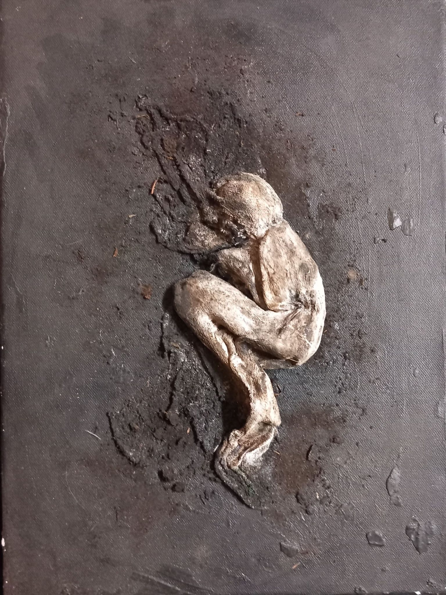 3d figure, in fetal poisition laying on the canvas which is dark and covered in earth, turf, the figure is plaster and  gauze,  she is shaded with ink.