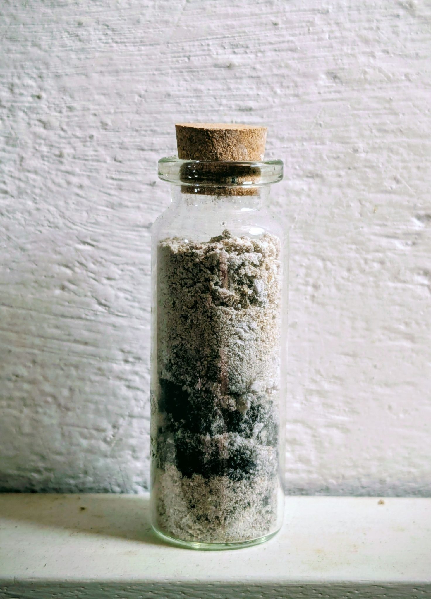 A small glass bottle filled with ash and charcoal pieces