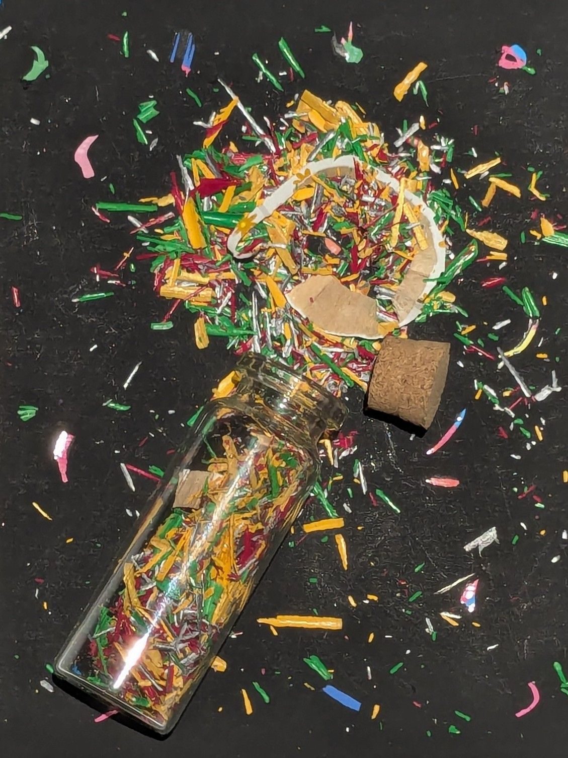A small glass bottle with an explosion of colours made by sharpened crayons on a black background