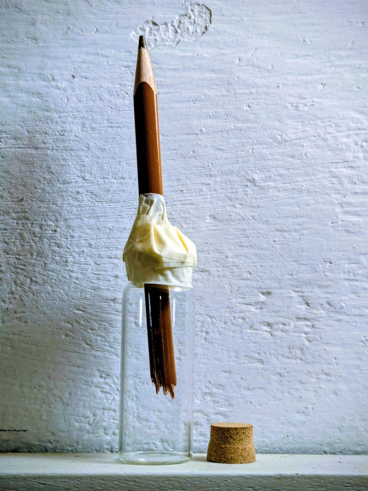 A small glass bottle containing a broken pencil secured with masking tape