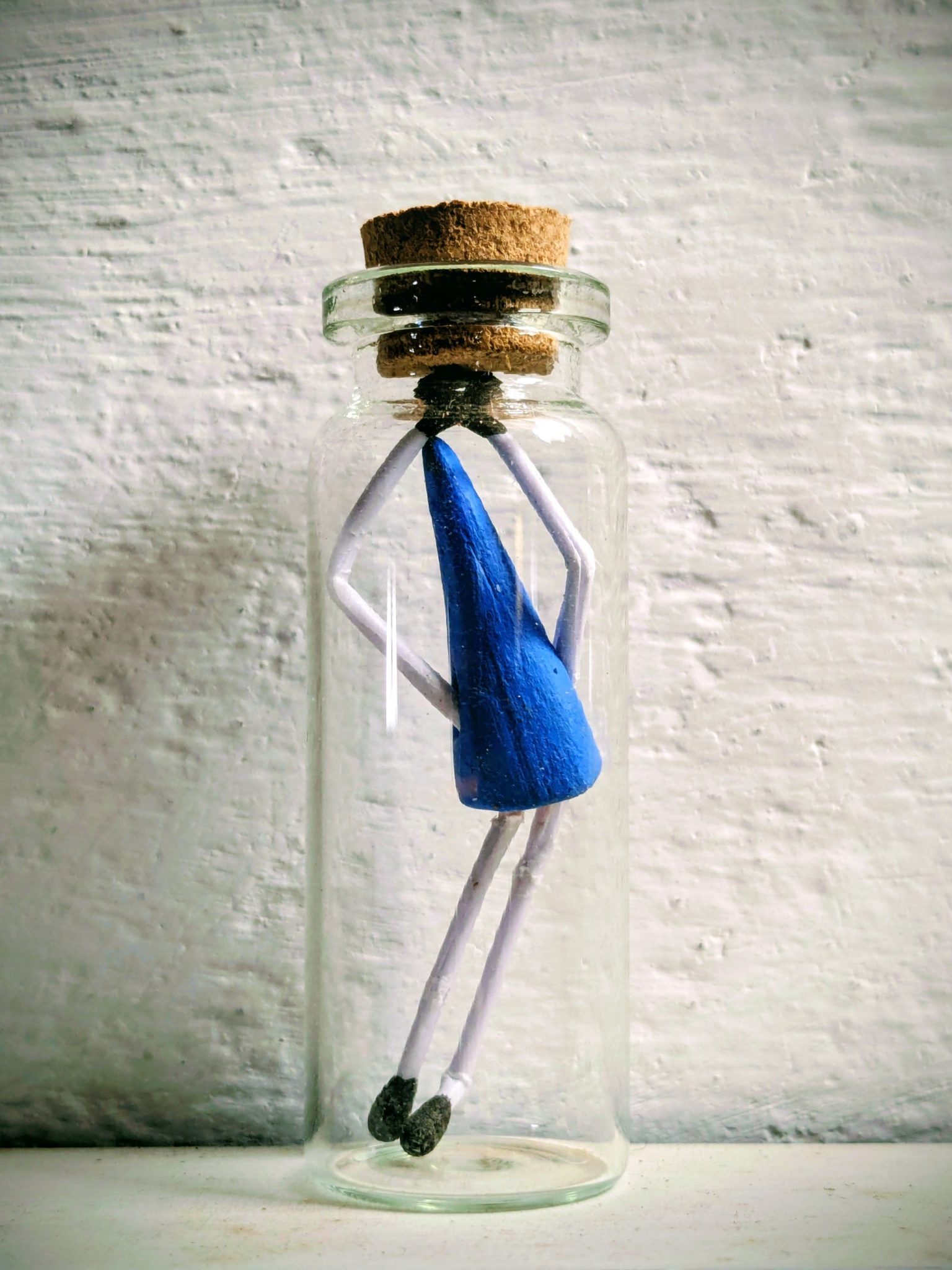 A small glass bottle contains a small figure shape made of a clay cone and match sticks, it looks like it's dancing